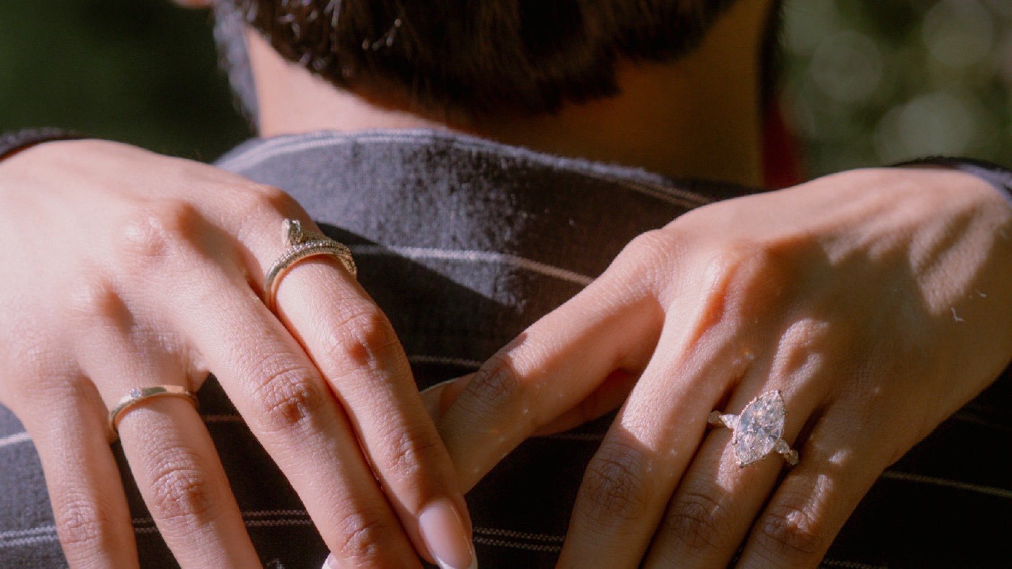 Hands resting on a shoulder, wearing a marquise engagement ring and stacked bands